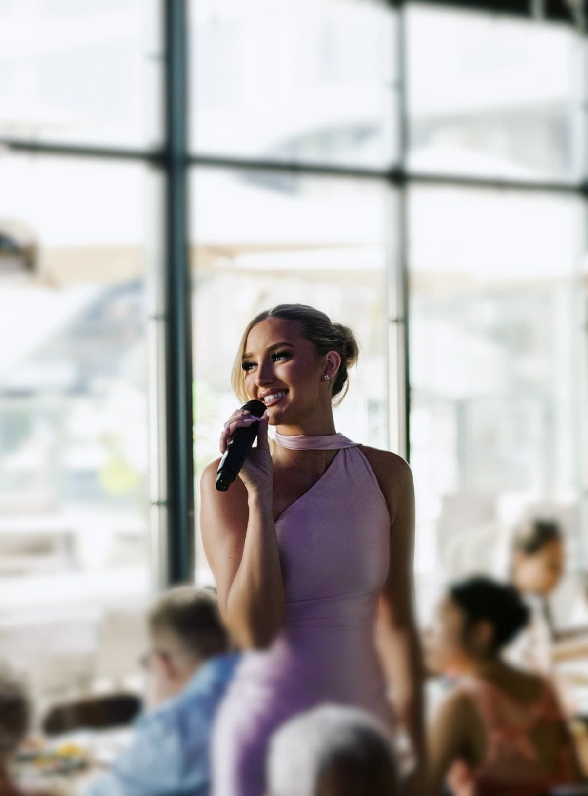 Dannii Murphy singing at a daytime event in front of tall windows